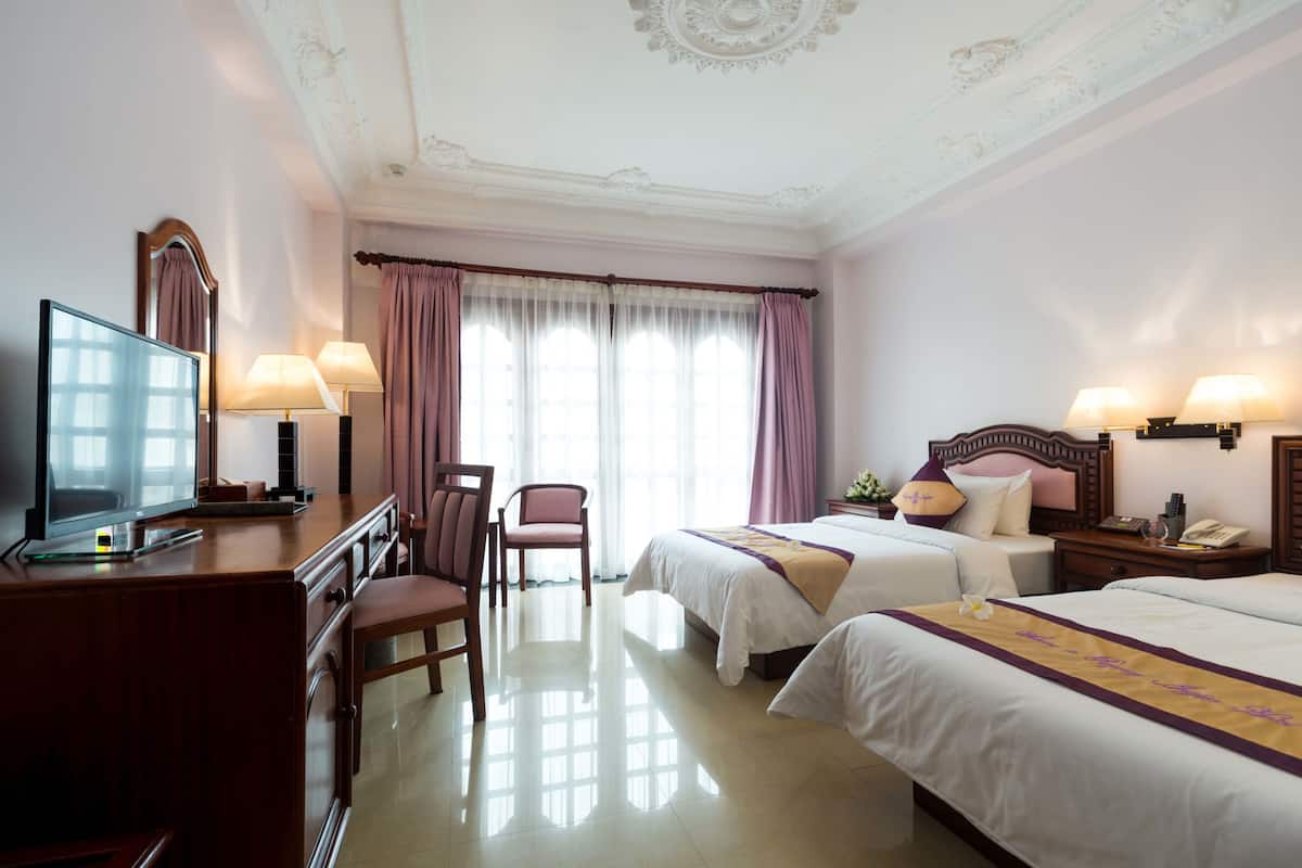 A hotel room with two beds, a desk with a television, a chair, and a nightstand with lamps.