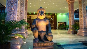 Una estatua de una figura sentada en un vestíbulo con columnas ornamentadas y plantas en macetas.