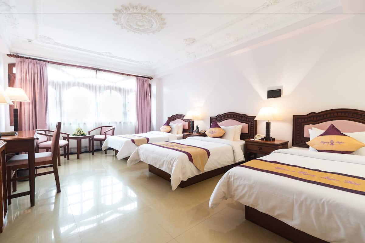 A hotel room with three beds, a dining table, chairs, and a large window with curtains.