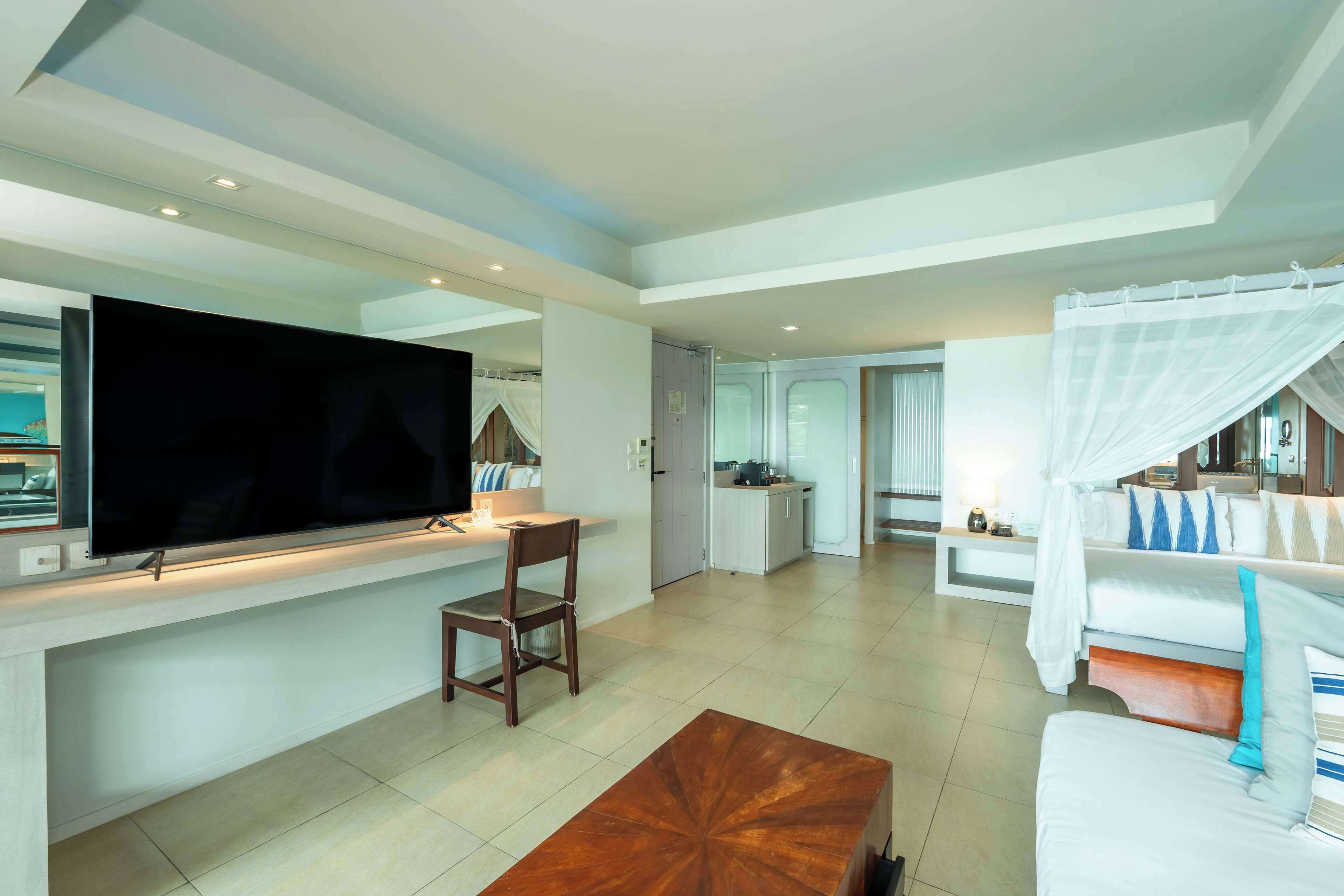 Et moderne hotelværelse med et fladskærms-tv, et spiseområde, en sofa og en seng med himmelseng.