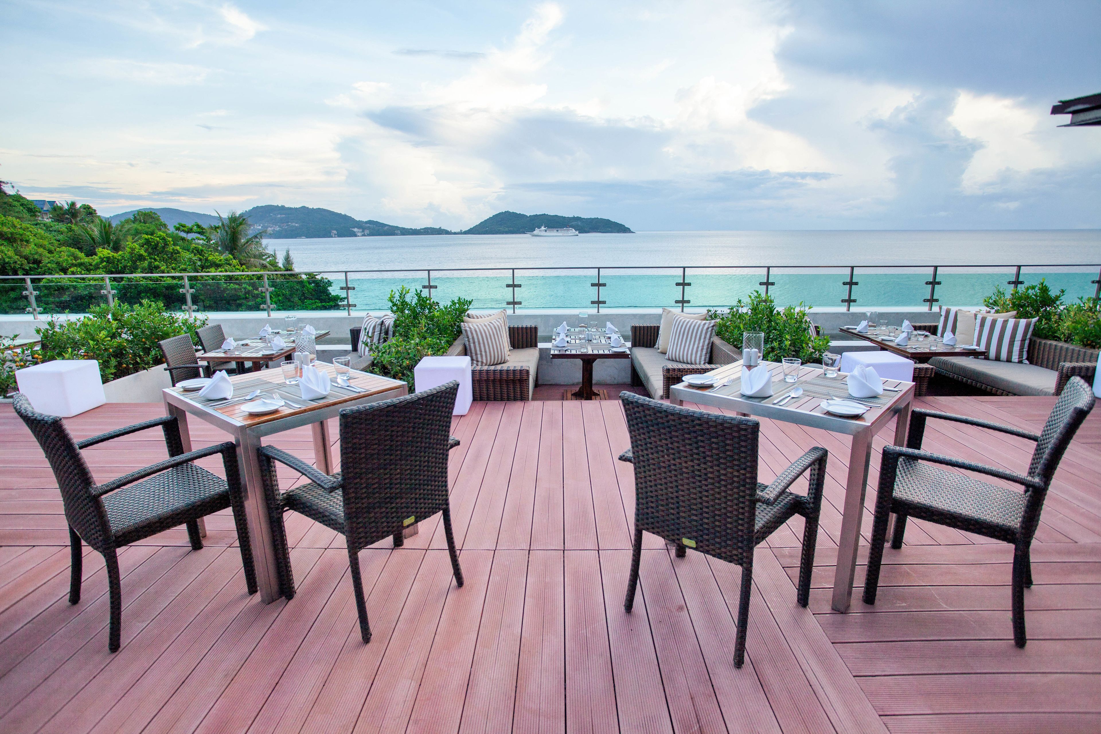 An outdoor dining area with tables and chairs, overlooking a body of water and distant land.