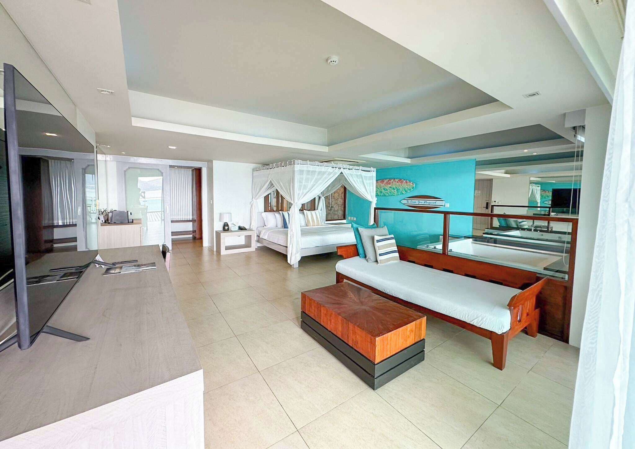 A hotel room with a large bed, a sofa, a TV, and a balcony with a view.