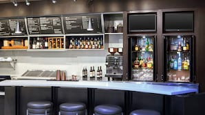 A bar area with a long counter, multiple stools, a coffee machine, and shelves stocked with bottles. - Courtyard by Marriott Wilmington Downtown/Historic District (Wilmington)