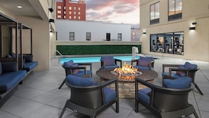 An outdoor patio with wicker furniture, a fire pit, and a pool in the background. - Courtyard by Marriott Wilmington Downtown/Historic District (Wilmington)