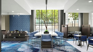 A modern hotel lobby with a large meeting table, blue chairs, a decorative tree, and large windows offering a view of the outdoors. - Courtyard by Marriott Wilmington Downtown/Historic District (Wilmington)