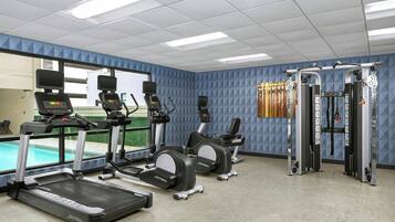 Une salle de sport équipée de tapis de course, de vélos elliptiques et d’appareils de musculation, avec de grandes fenêtres et une vue sur une piscine.
