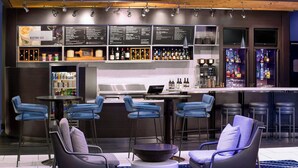 Zona de bar moderna con tablero de menú, taburetes y un área de estar con sillas y una mesa redonda.