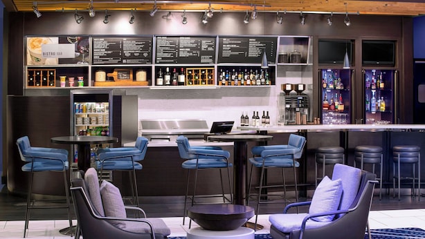 A modern bar area with a menu board, bar stools, and a seating area with chairs and a round table. - Courtyard by Marriott Wilmington Downtown/Historic District (Wilmington)