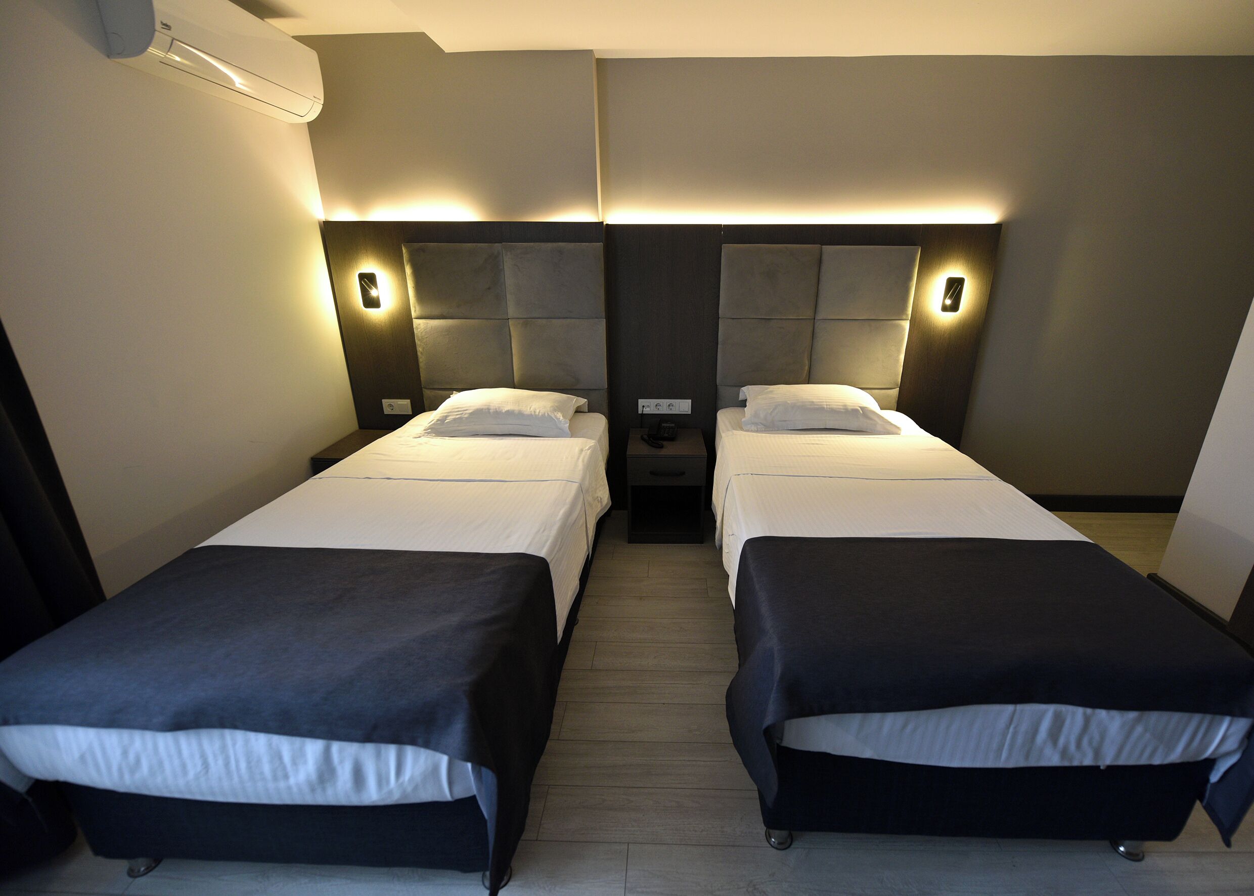 Habitación doble con dos camas, una mesita de noche con teléfono y aire acondicionado de pared.