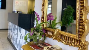 A reception desk with a gold-framed mirror, a vase with purple flowers, and a magazine rack. - Sahil Hotel Pendik (Istanbul)