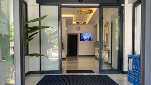 A modern hotel entrance with glass doors, a black mat, a TV screen, and a blue information kiosk. - Sahil Hotel Pendik (Istanbul)