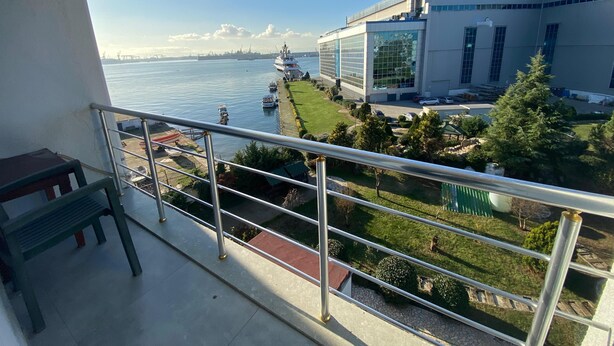 A balcony with a view of a river, a large building with glass windows, and a grassy area with trees. - Sahil Hotel Pendik (Istanbul)