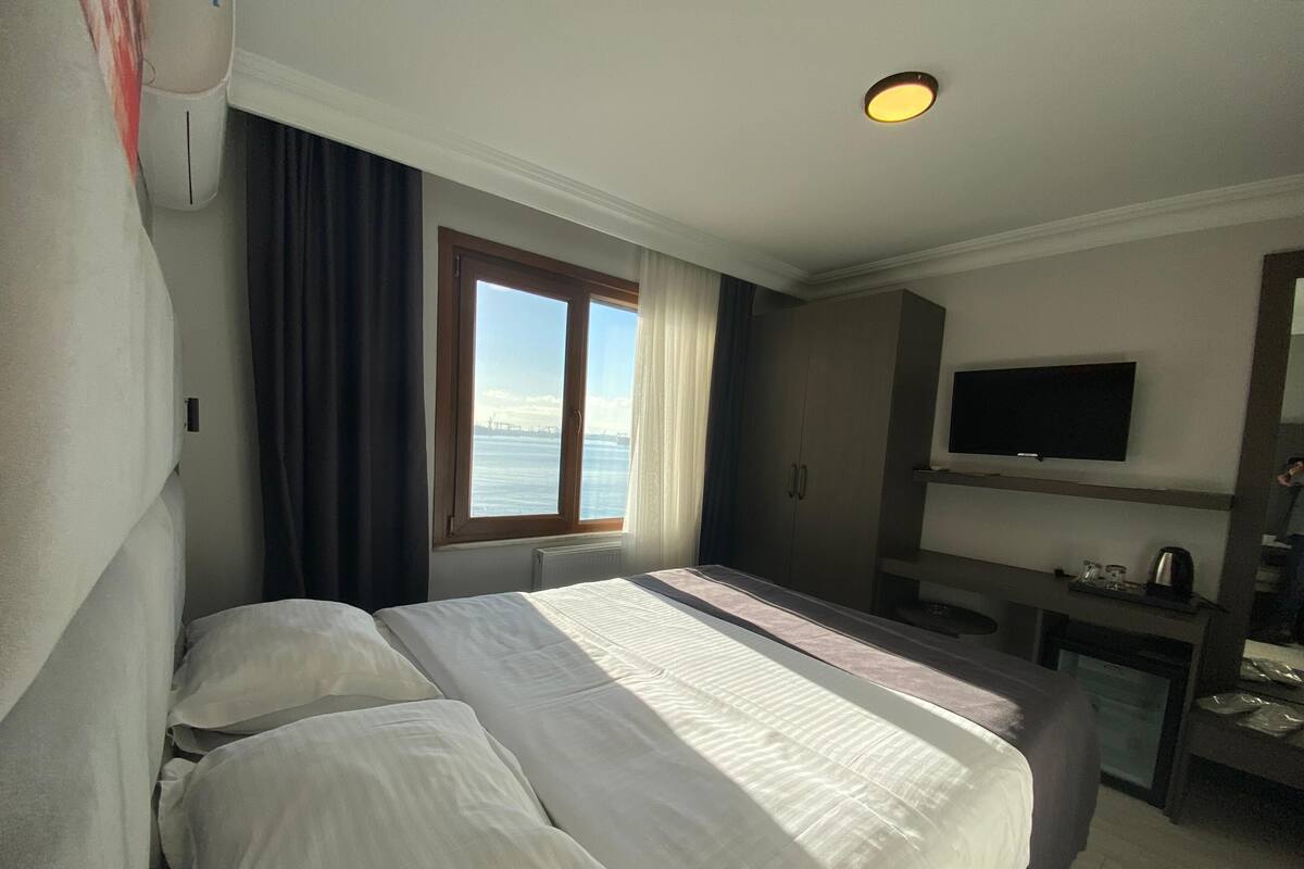 Une chambre d’hôtel avec un lit, un bureau, une télévision et une fenêtre donnant sur la mer.