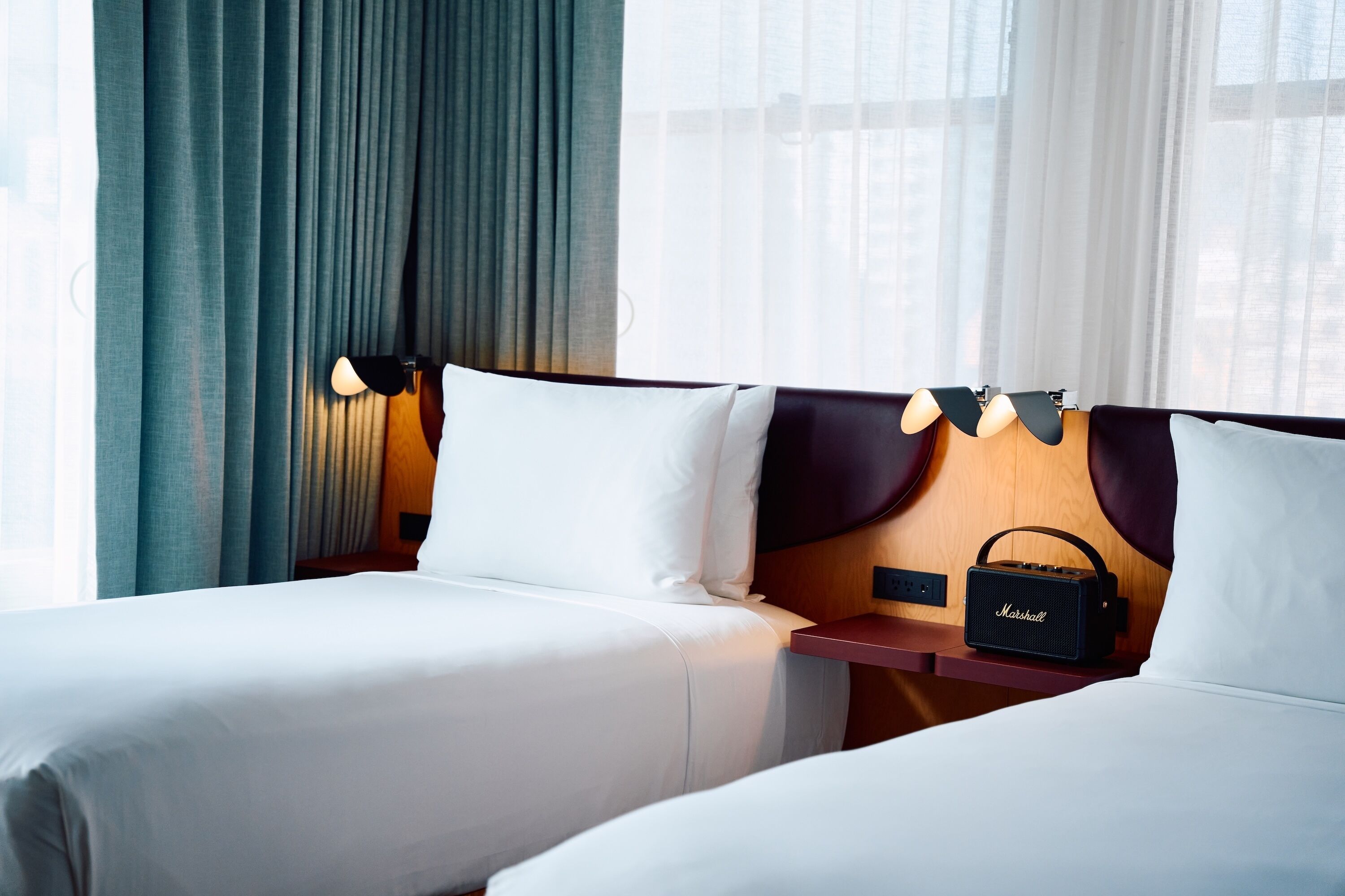 A hotel room with two beds, a Marshall speaker, and a window with curtains.
