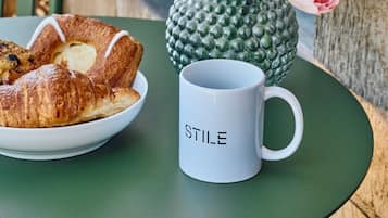 Una mesa con un plato de croissants, un florero con forma de piña y tulipanes rosados, y una taza con la palabra 'STILE'.
