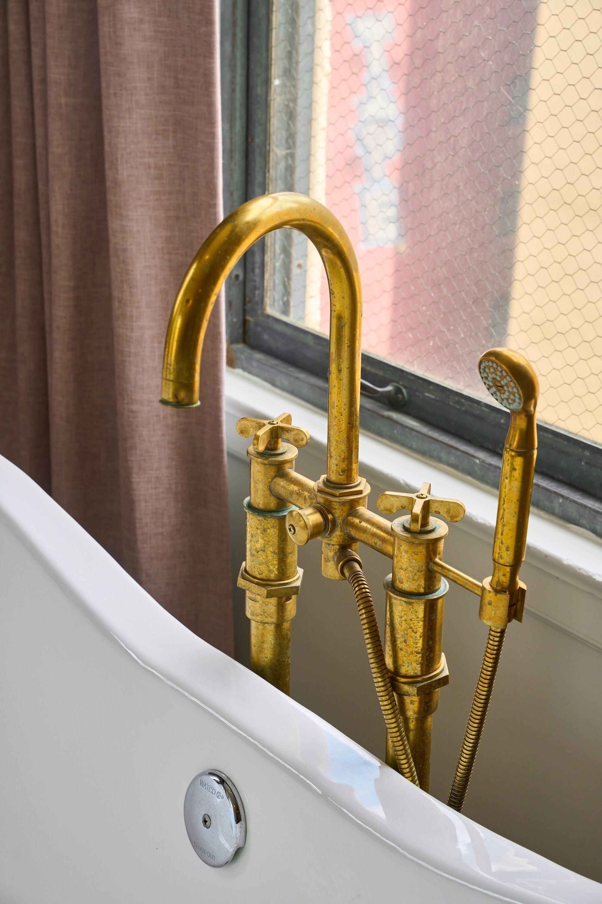 A bathtub with brass fixtures and a window with a view of a building.