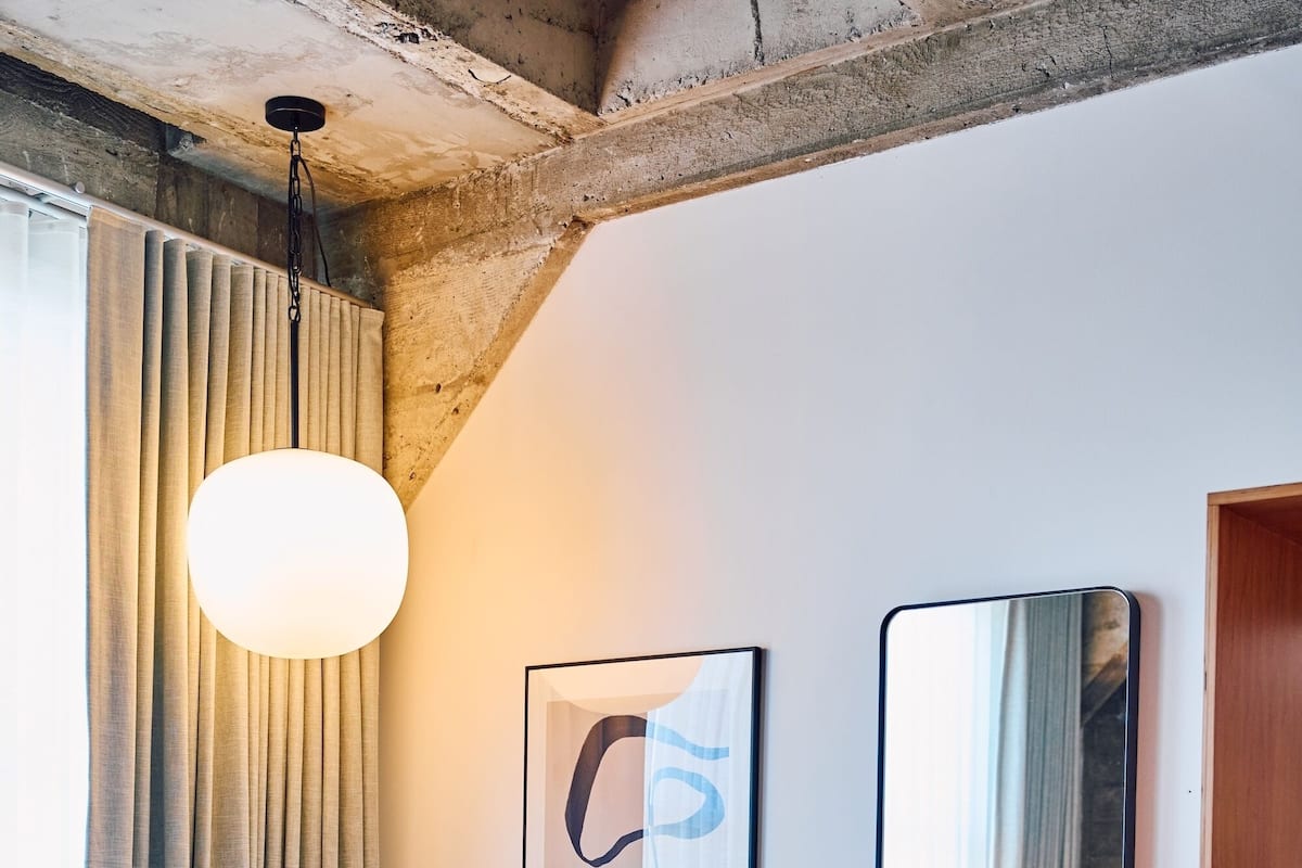 Hotellihuone, jossa on sänky, tuoli, suuri peili, seinälle kiinnitetty taideteos ja kuviollinen matto.