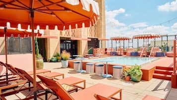 Un espace piscine aménagé sur le toit, avec des chaises longues, des parasols et des plantes en pot.