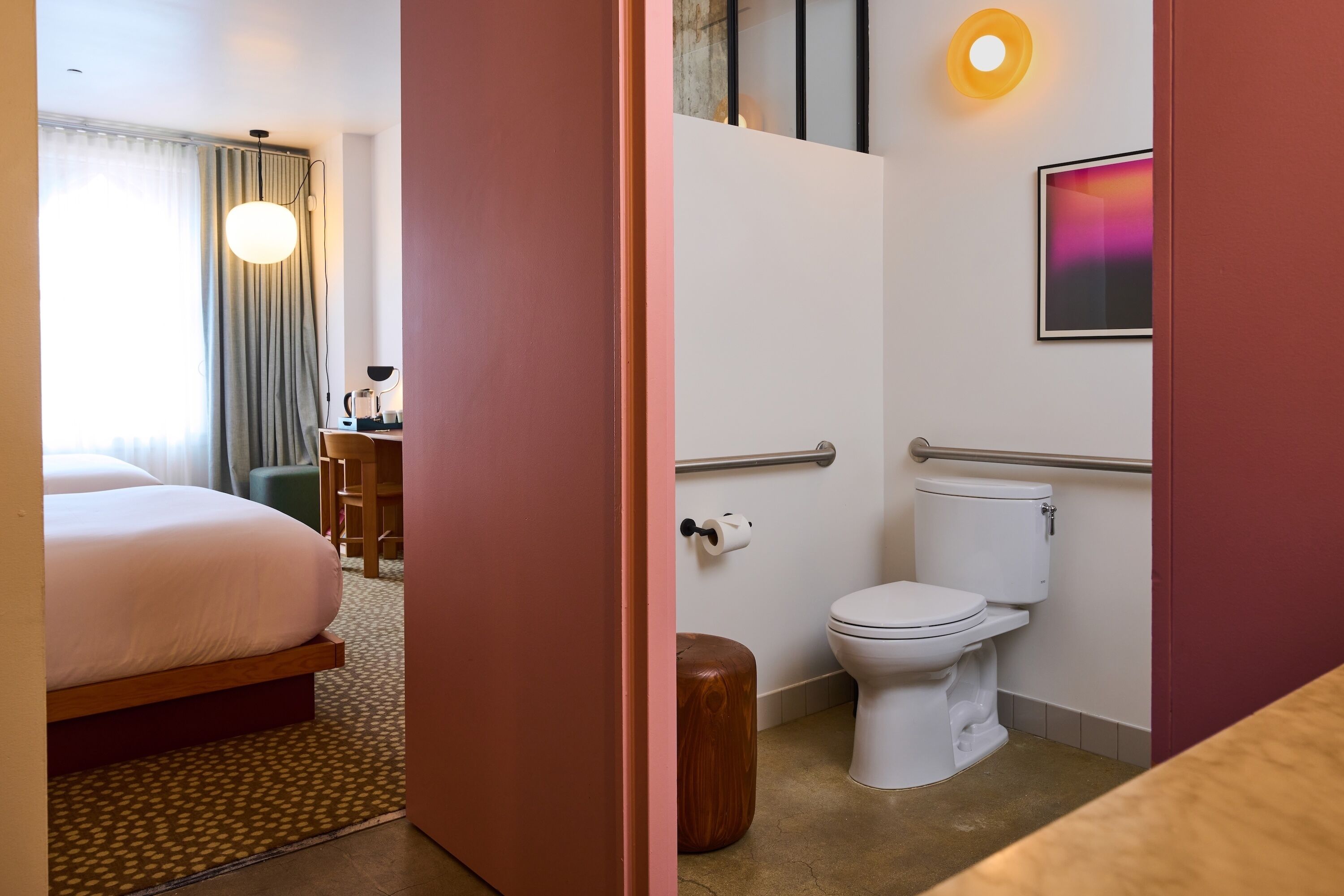 Habitación de hotel con cama, baño con inodoro, zona de ducha y un taburete de madera.