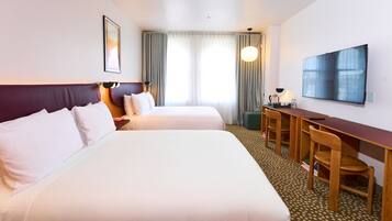 Une chambre d’hôtel avec deux lits, un bureau avec des chaises, une télévision et une fenêtre avec des rideaux.
