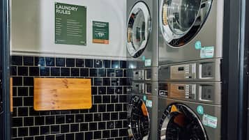 A laundry facility with multiple washing machines, a wooden signboard, and a tiled wall.
