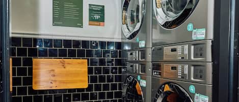 A laundry facility with multiple washing machines, a wooden signboard, and a tiled wall.