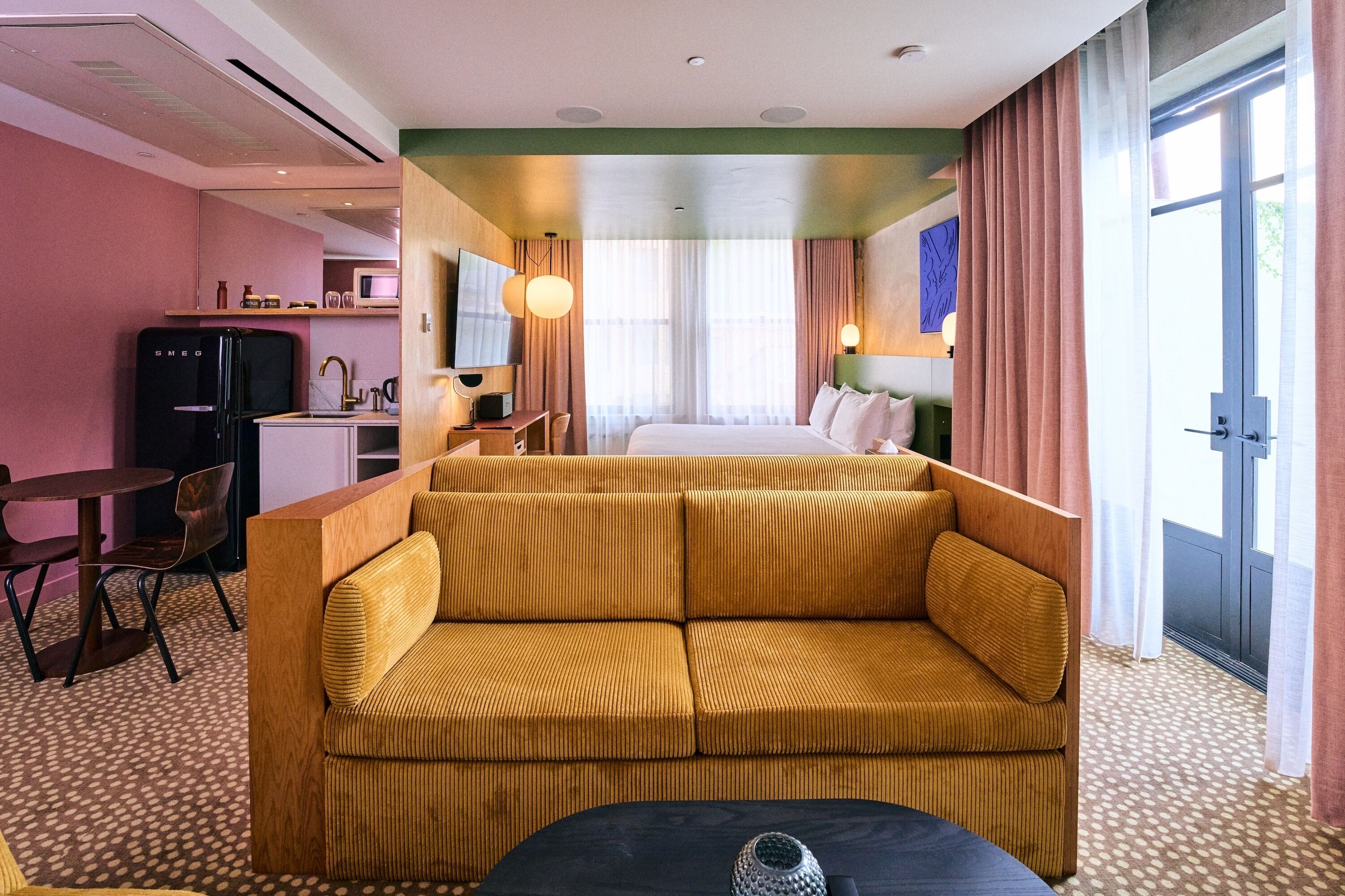 Ett hotellrum med en soffa, ett matbord, ett litet köksutrymme och en säng.