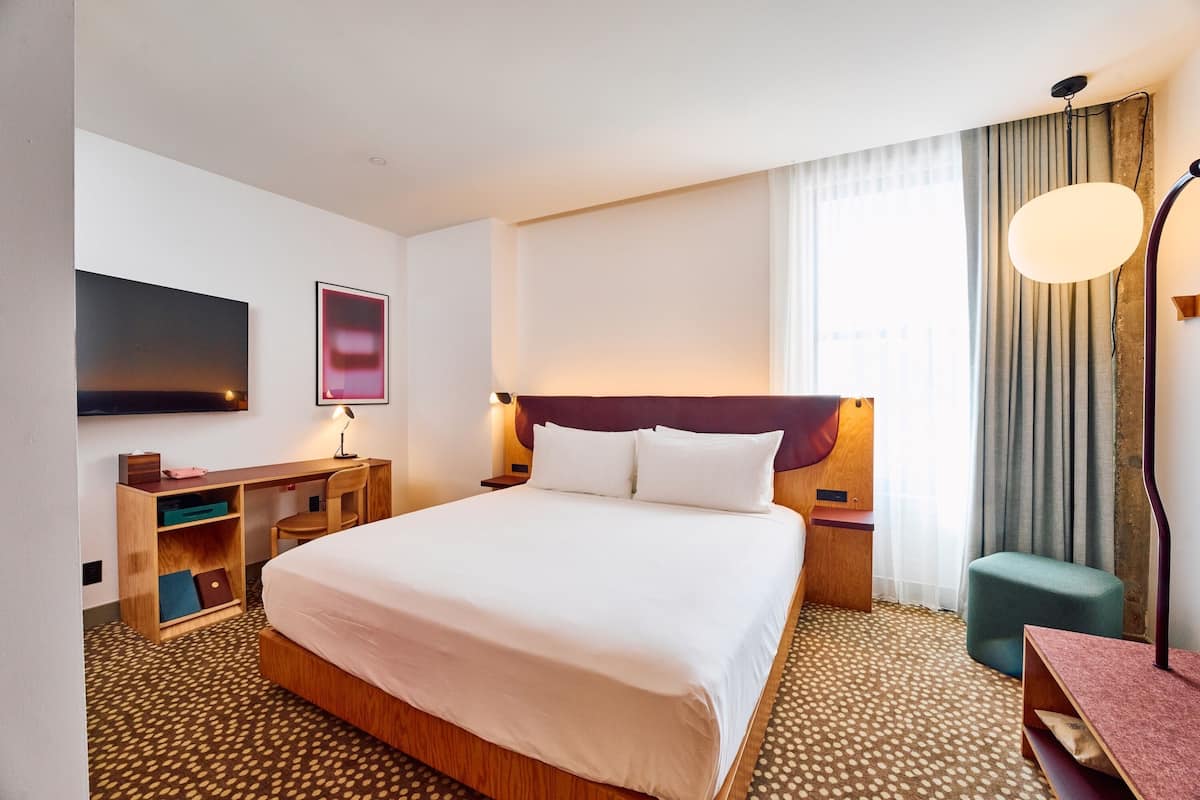 Hotellihuone, jossa on suuri sänky, työpöytä, tuoli, televisio ja lamppu.