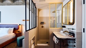 A hotel room with a bed, a shower, a sink, and a mirror.