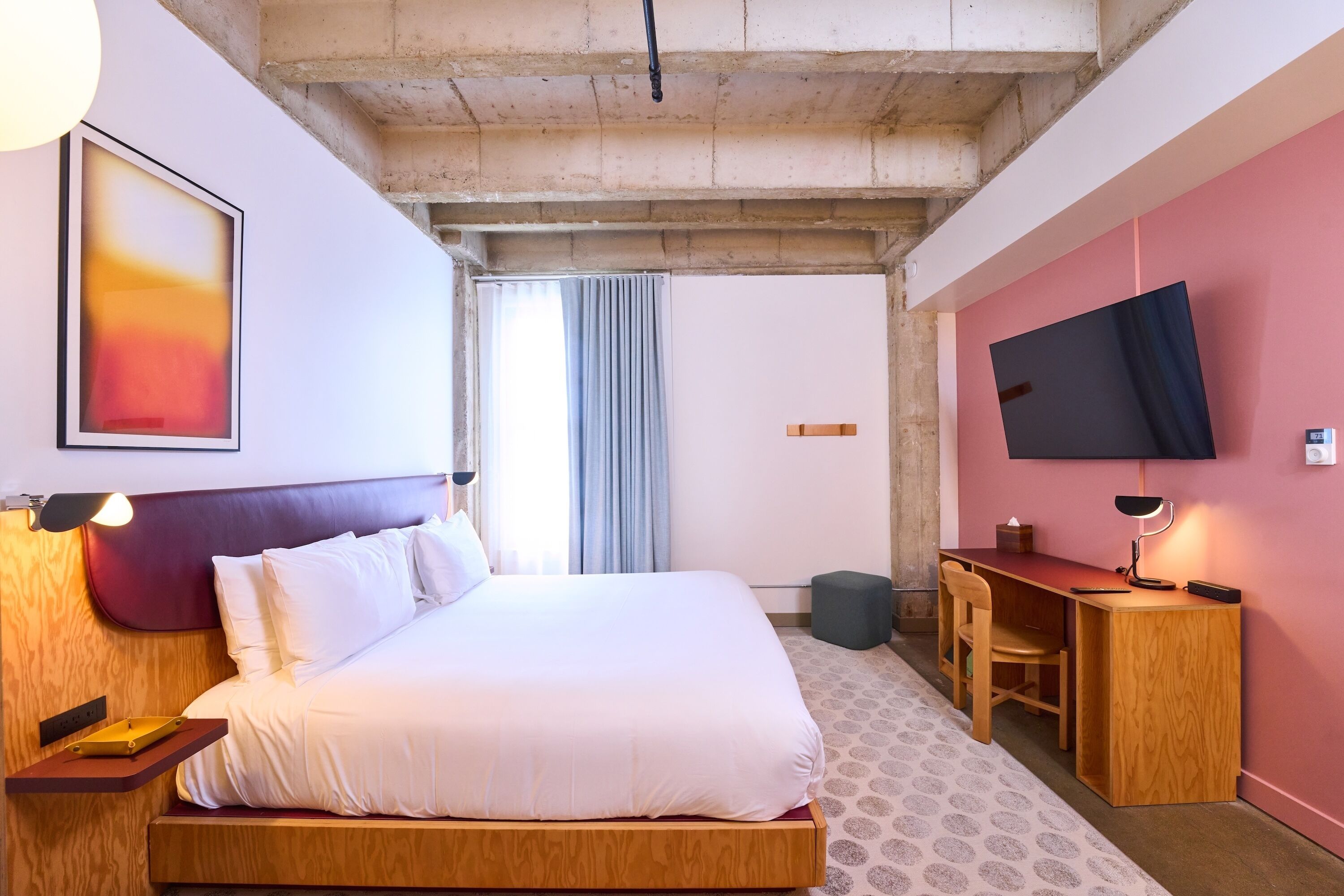 Een hotelkamer met een bed, bureau, stoel, televisie en kunstwerk.