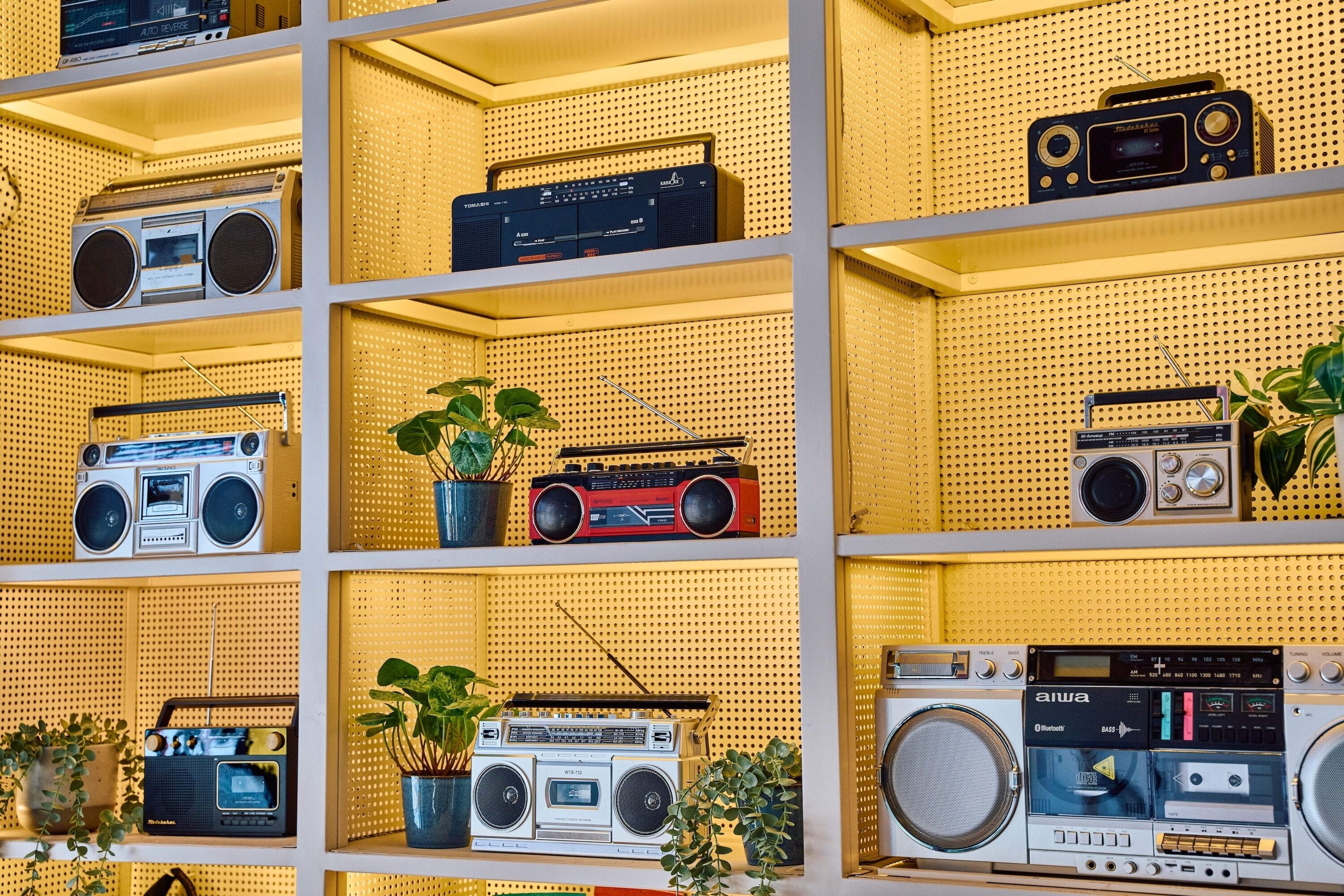 A wall with multiple shelves displaying various vintage radios.
