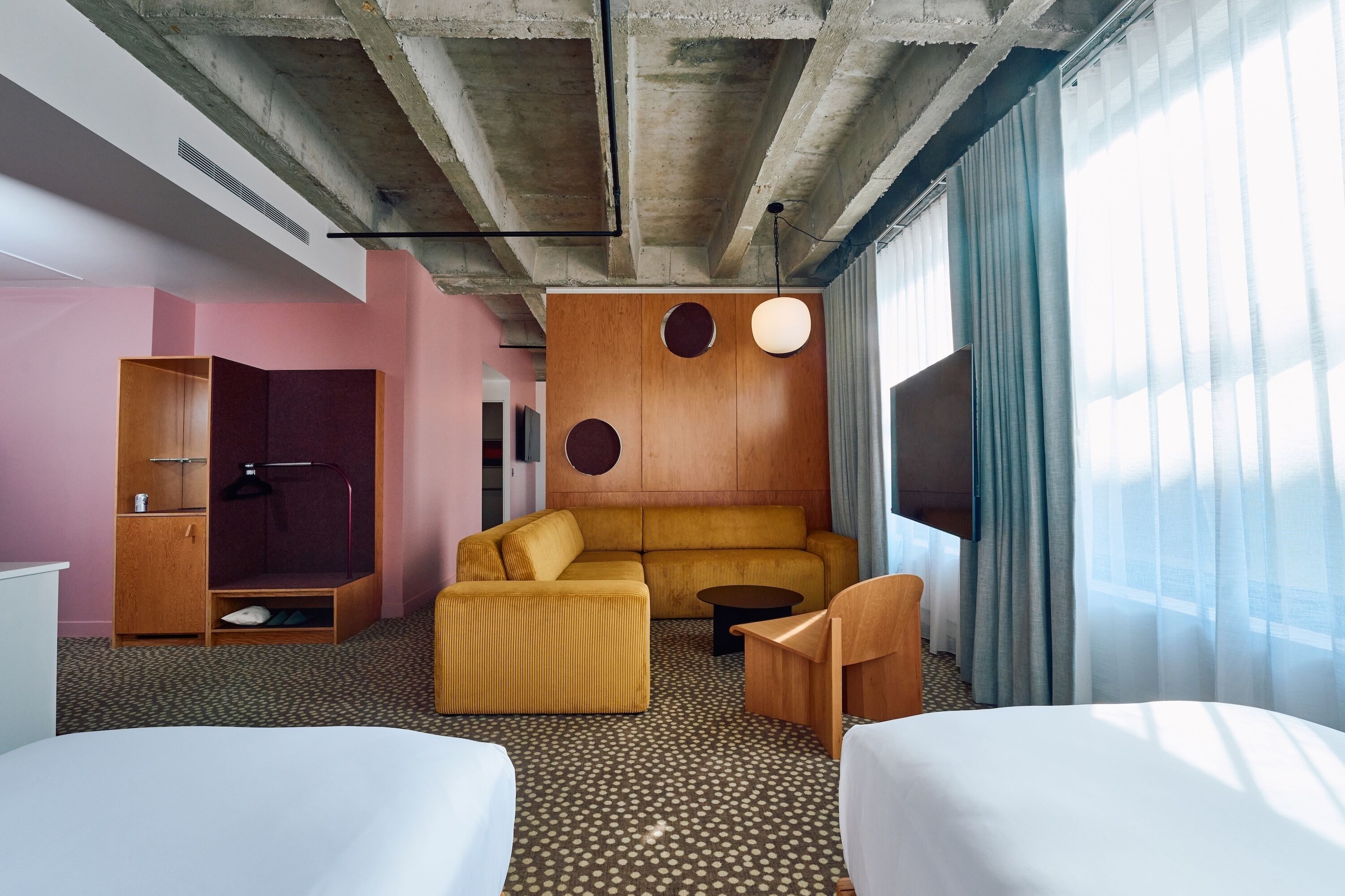 A hotel room with a sofa, two single beds, a wooden wardrobe, a small table, and a TV.