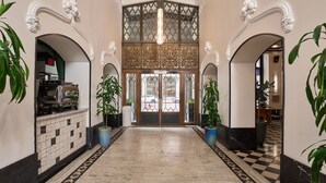 A hotel lobby with ornate architecture, a checkered floor, and potted plants.