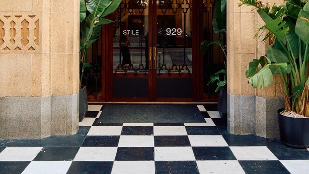 A building entrance with ornate carvings, a sign reading 'STILE,' and a checkered floor.