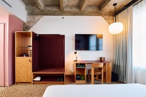 Hotellihuone, jossa on sänky, työpöytä tuolilla, vaatekaappi, televisio ja riippuvalaisin.