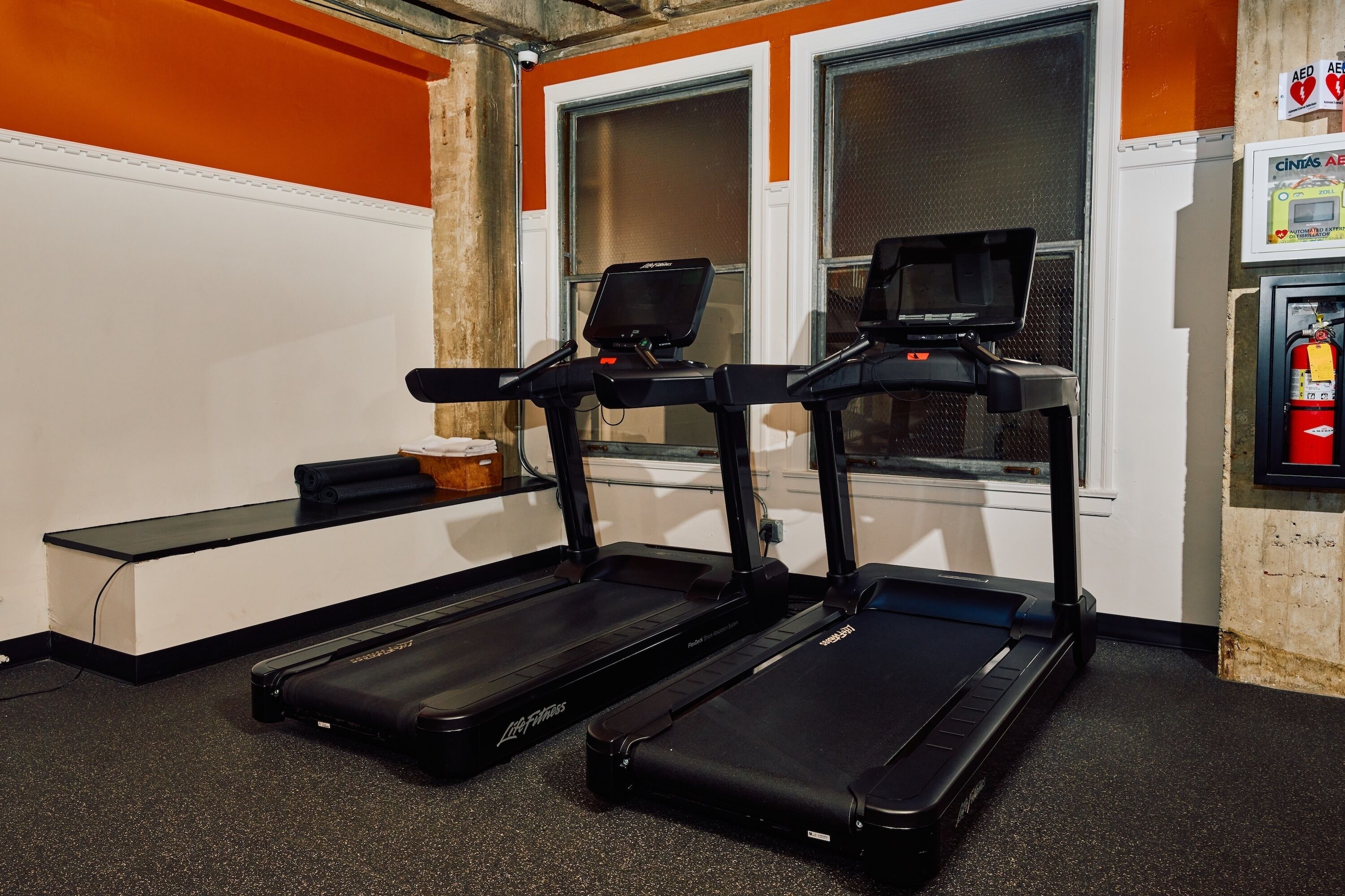 Deux tapis de course, un banc et une fenêtre avec des murs orange.