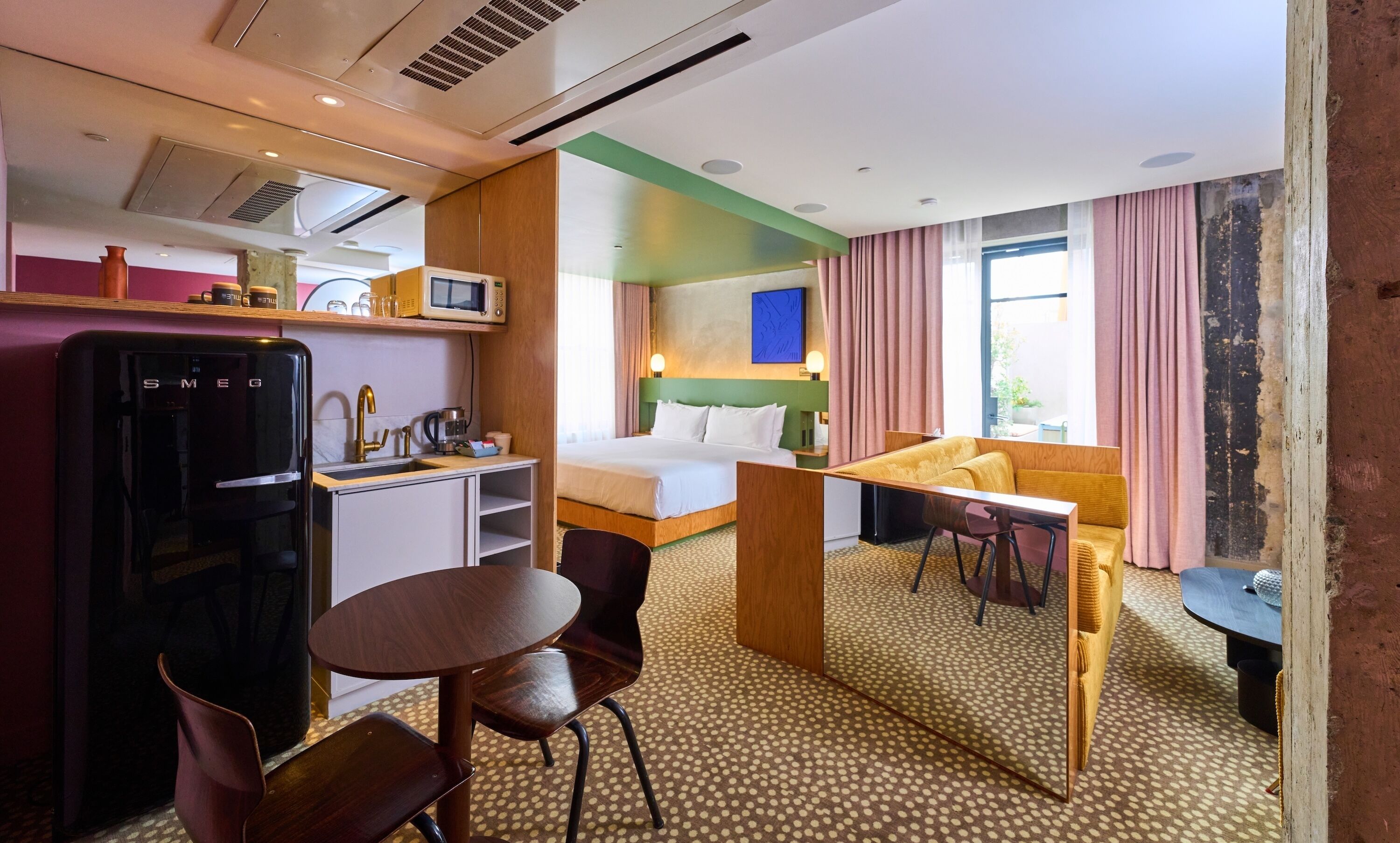A compact hotel room with a kitchenette, a bed, a sofa, and a dining area.