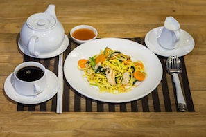 A table set with a teapot, cup, saucer, bowl of soup, a plate of noodles, and cutlery.