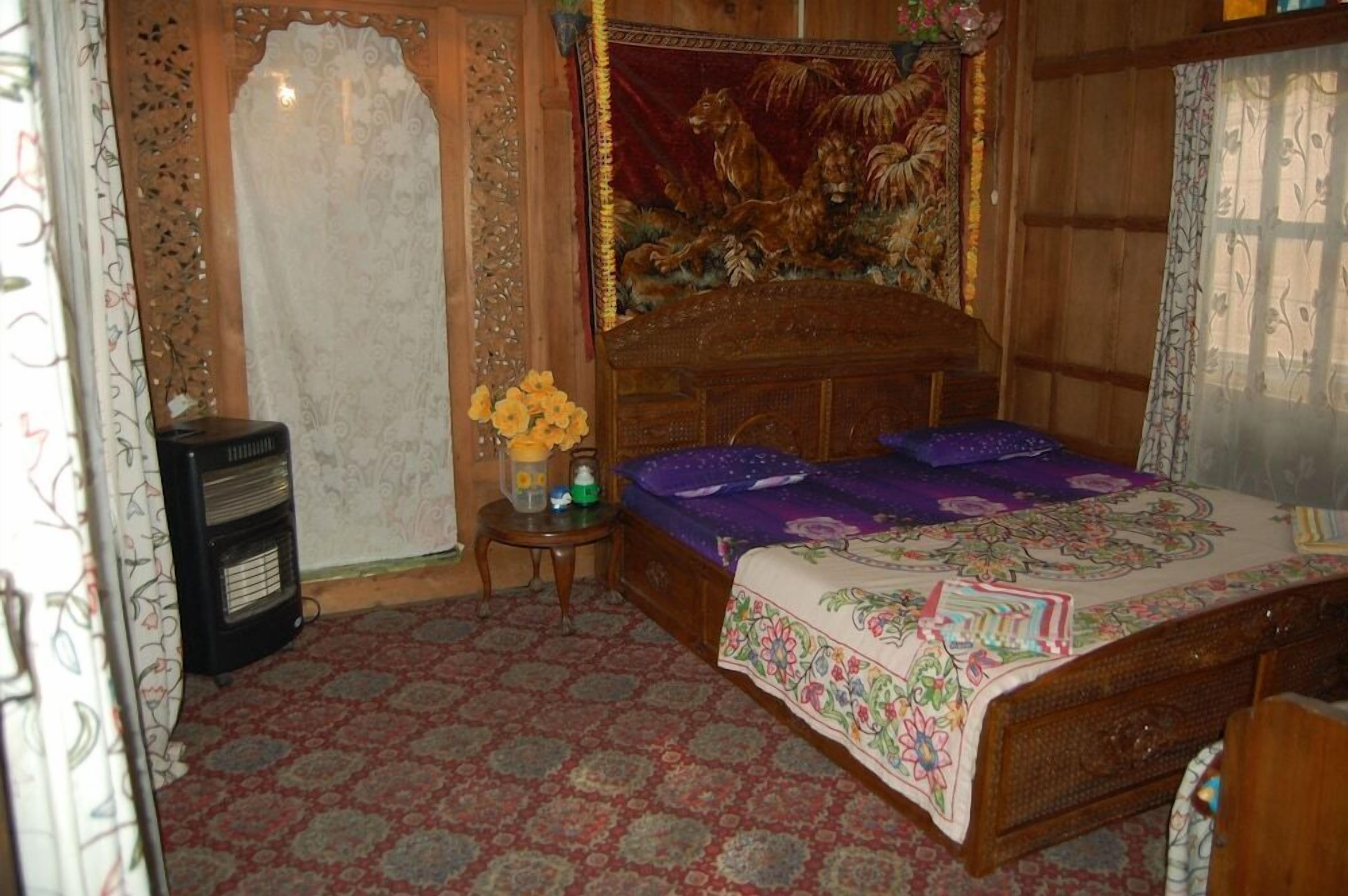 Una habitación con una cama, un calentador, una mesita con flores y un tapiz en la pared.