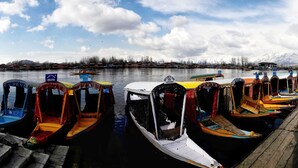 A row of colorful boats docked at a pier with a calm lake and mountains in the background. - Houseboat Zaindari Palace (Srinagar)