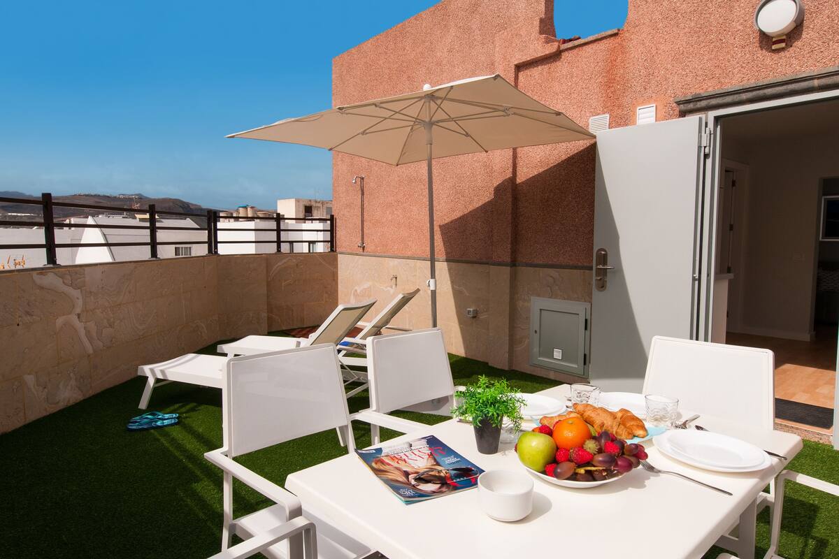 Eine Dachterrasse mit einem für ein Frühstück gedeckten Tisch, darunter Obst, Brot und eine Zeitschrift.