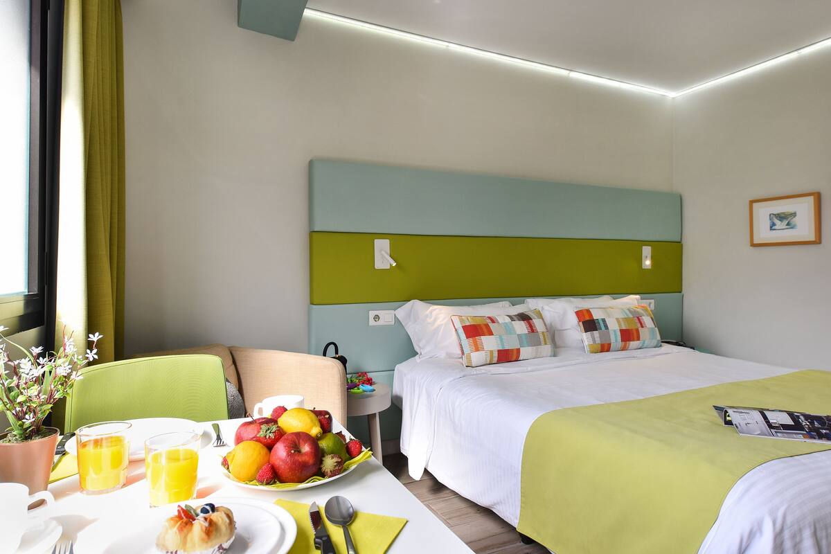 Ein Hotelzimmer mit Bett, Nachttisch, Frühstückstisch und einem Fenster mit Vorhängen.