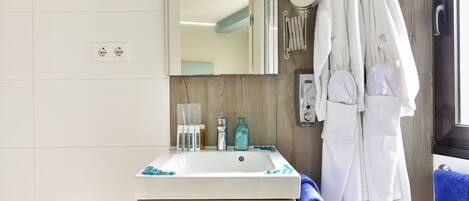 A bathroom with a white sink, wooden vanity, and a mirror above it. There are towels and toiletries on the counter.