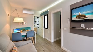 A modern living room with a sofa, a dining area with a laptop, and a TV displaying a beach scene. - Hotel Apartamentos Bajamar (Las Palmas de Gran Canaria)