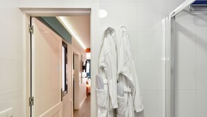 A hotel hallway with a glass shower door, white tiled walls, and a pair of white robes hanging on a rack. - Hotel Apartamentos Bajamar (Las Palmas de Gran Canaria)