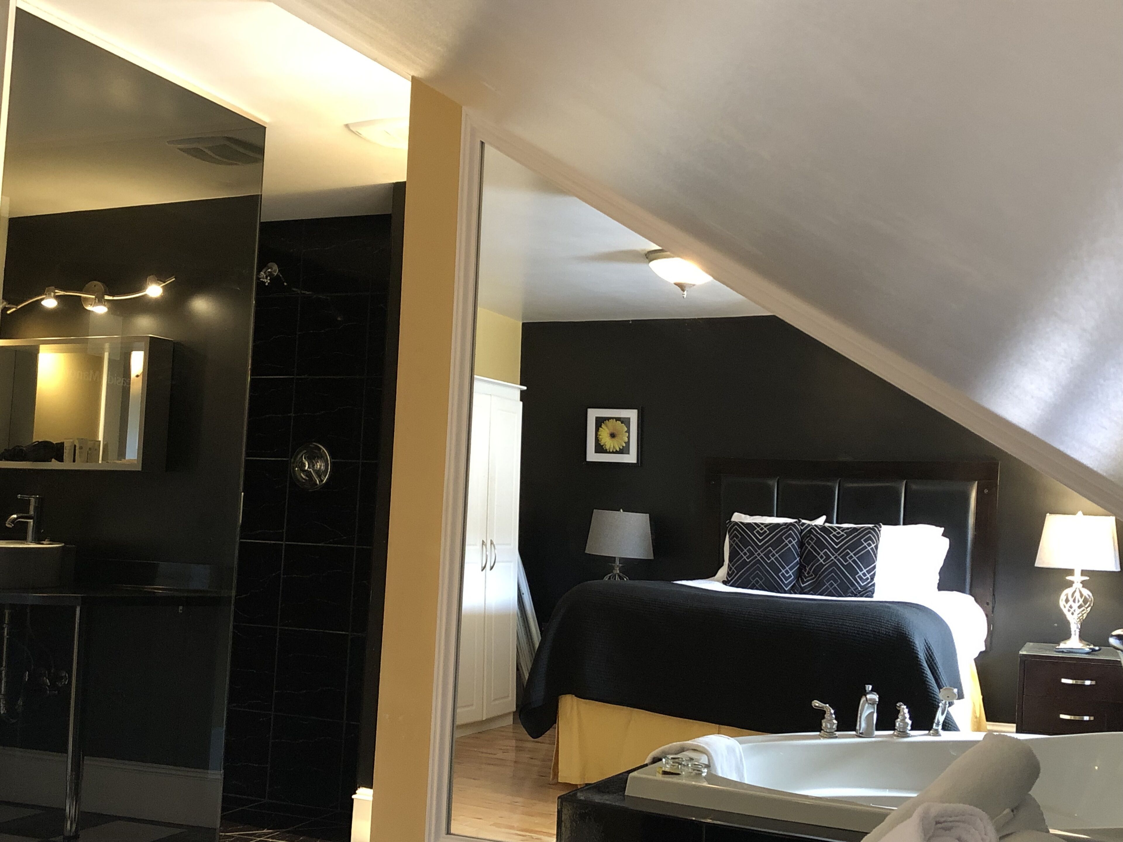 Et moderne hotelværelse med en stor seng, eget badeværelse, et sminkebord med spejl og et lille natbord med lampe.