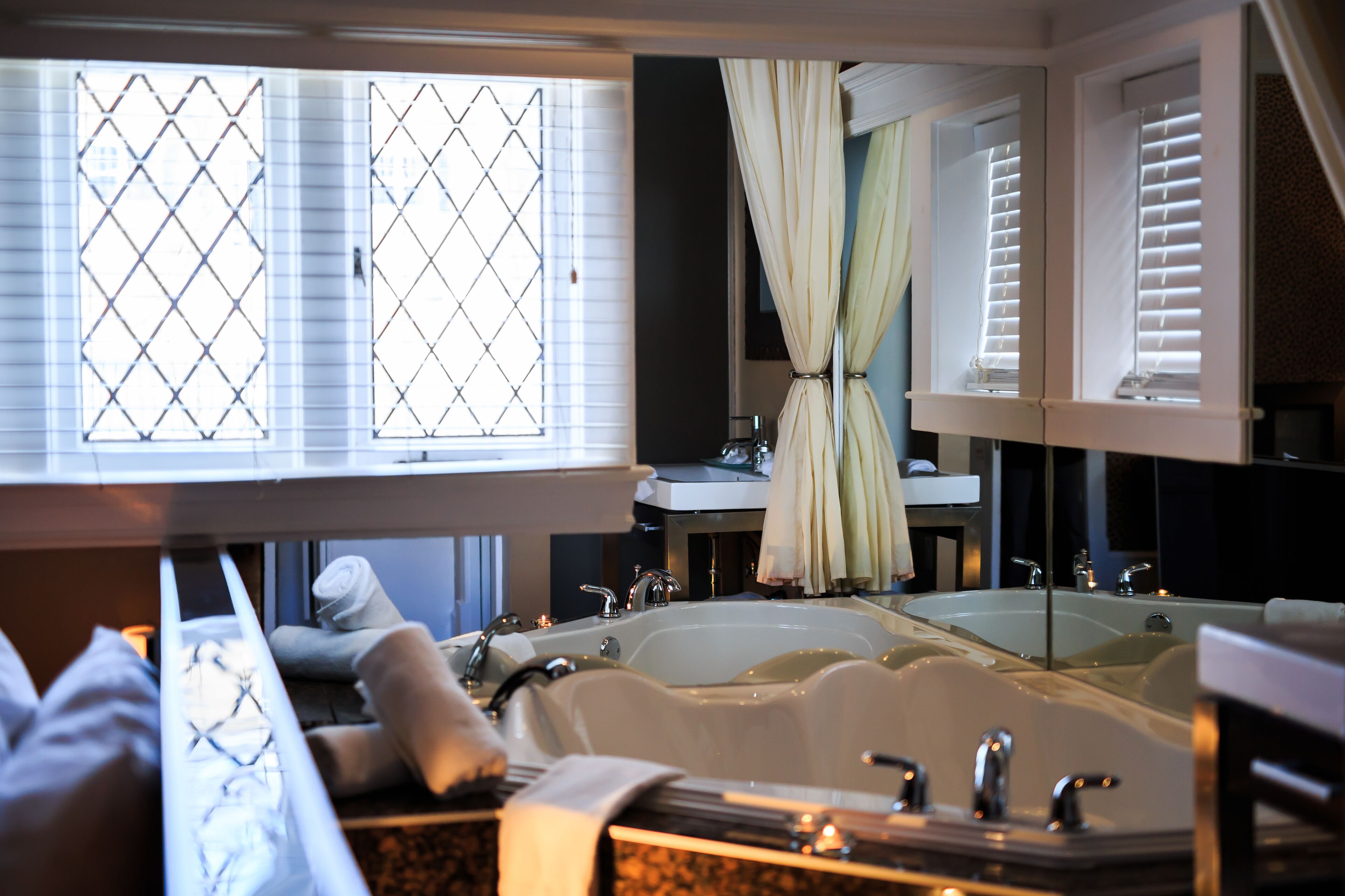 A bathroom with a large bathtub, a mirror, and a window with blinds.