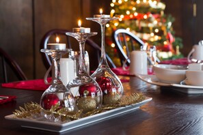 A table set with three glass candle holders, red and gold ornaments, and a white plate with a gold leaf centerpiece. - Leaside Manor by The Leaside Group (St. John's)