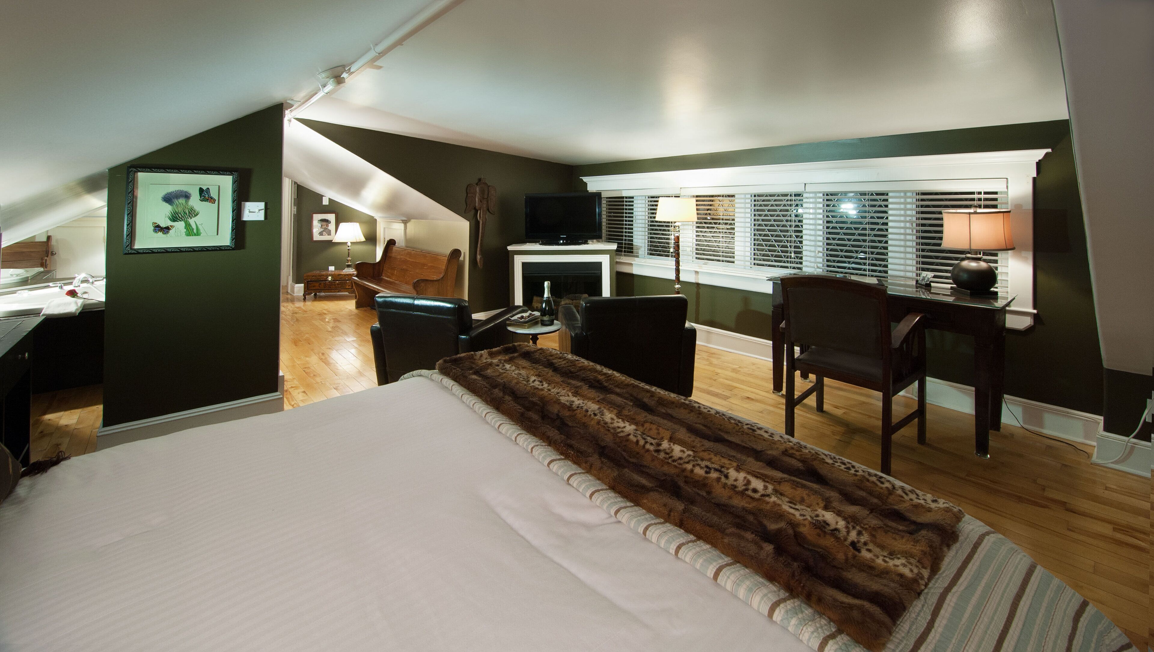 A bedroom with a large bed, a desk, a chair, and a fireplace.