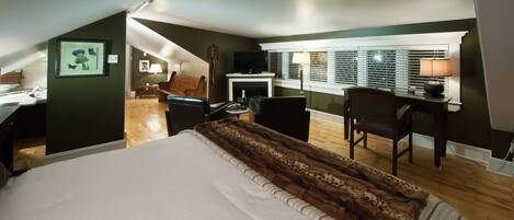 A bedroom with a large bed, a desk, a chair, and a fireplace.